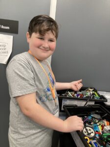 A kid smiles in front of Lego EV3 tubs 