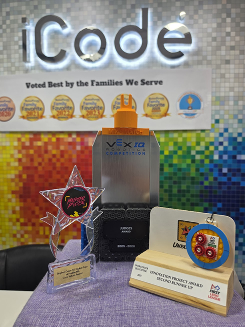 A competition robot on a tournament field beside a trophy and a team record