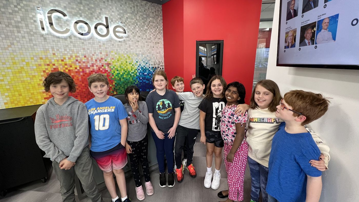 Smiling iCode students in front of the iCode sign