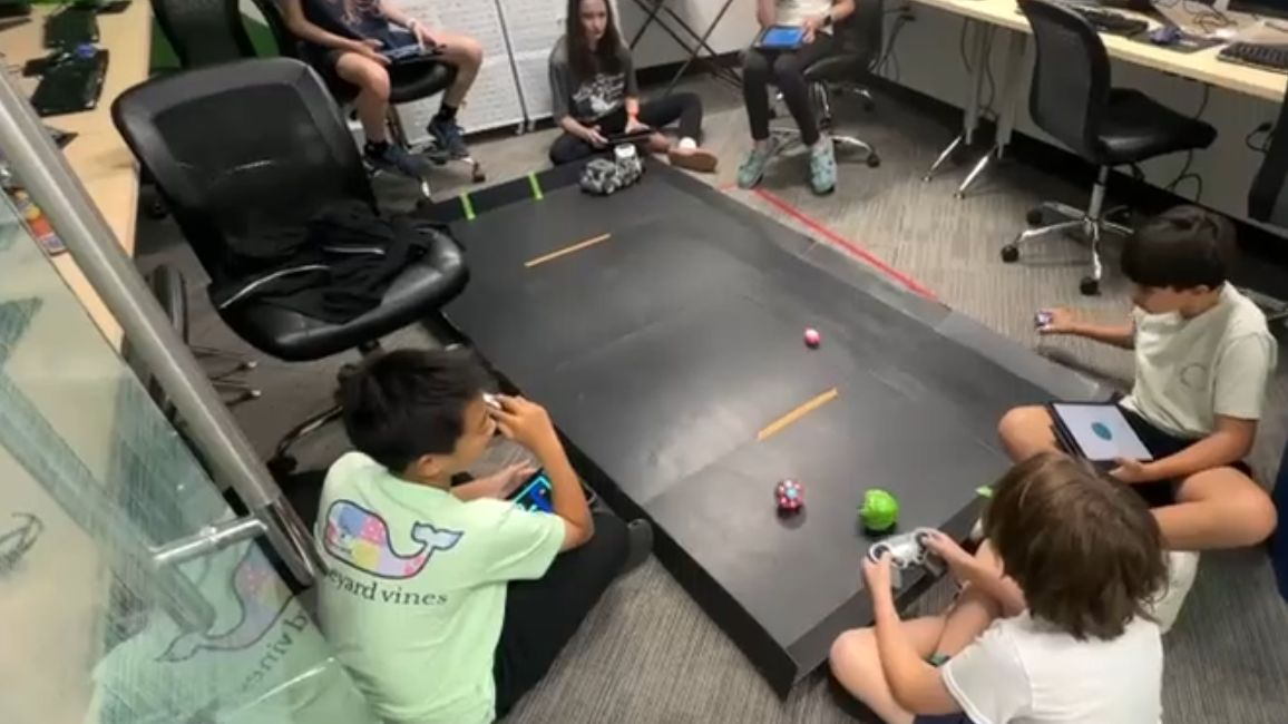 Students driving robots they programmed across the classroom floor